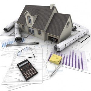A house on top of a table with mortgage application form, calculator, blueprints, etc..